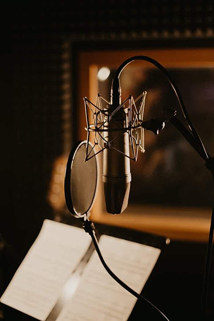 Anasayfa Close-up of a microphone and pop filter in a dimly lit recording studio, perfect for music production.